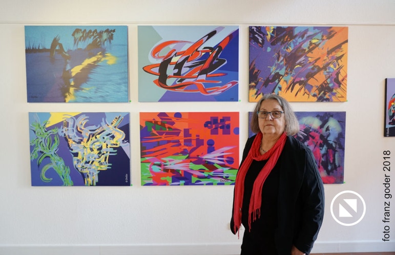 Dorothea Goder präsentiert ihre Bilder vor einer Bilderwand zur Austellung "Fantastische Welten"